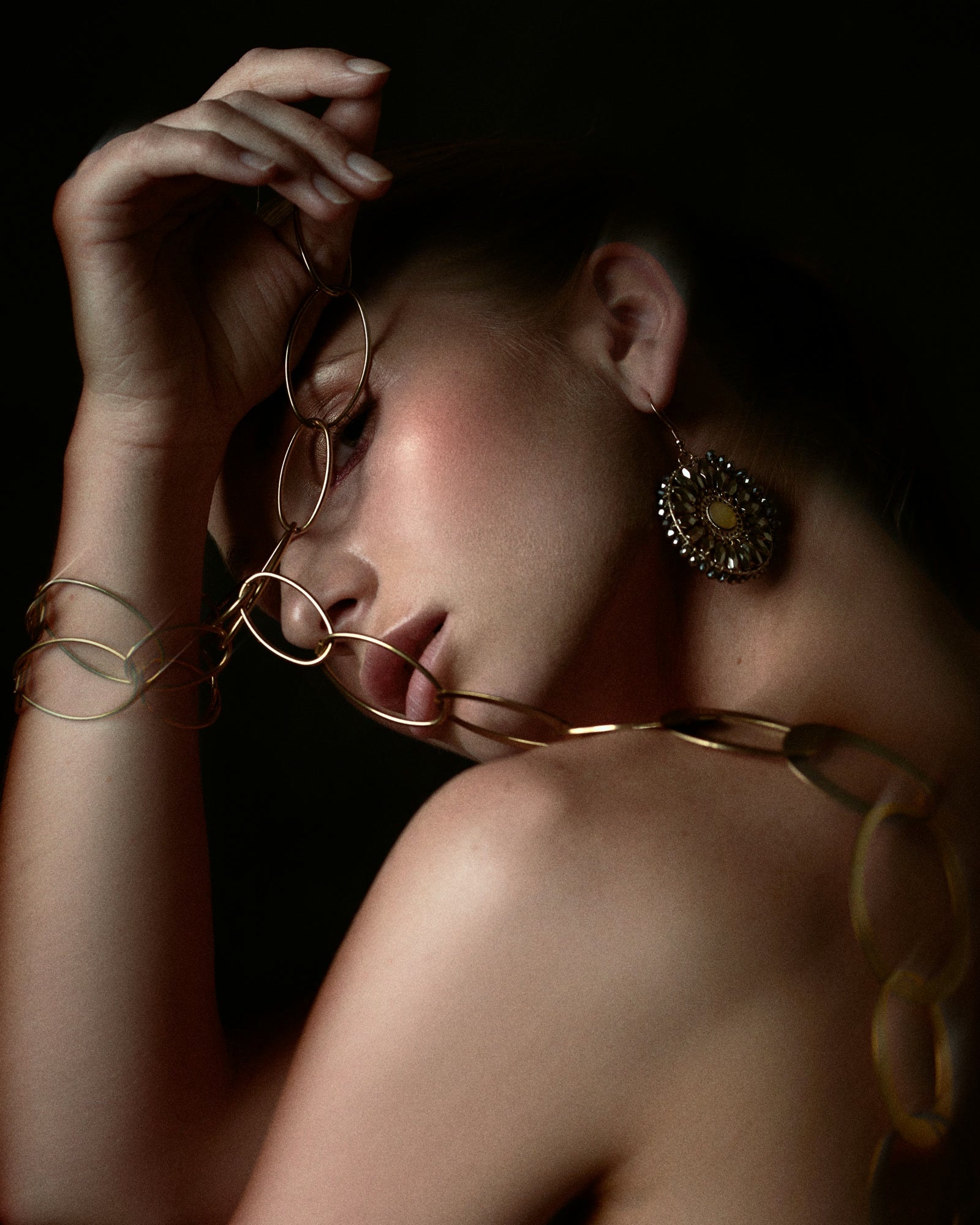 She turns into darkness, a gold chain looping past her lips and a disc earring catching the light.