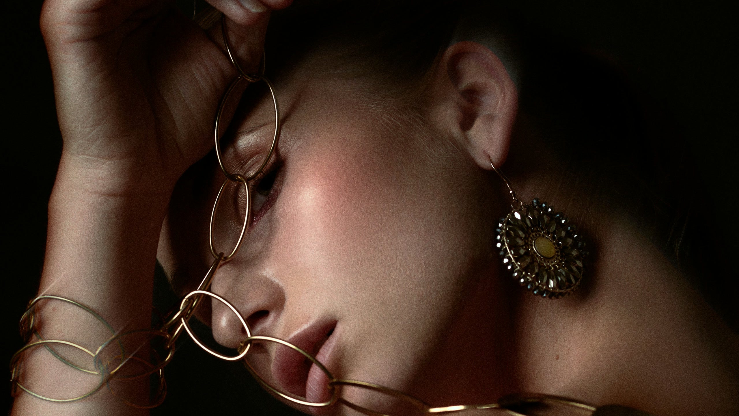 She turns into darkness, a gold chain looping past her lips and a disc earring catching the light.