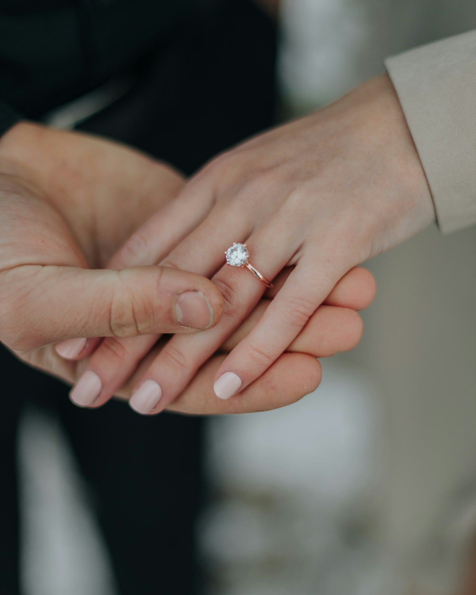 Two hands rest together, a solitaire diamond ring on her ring finger.